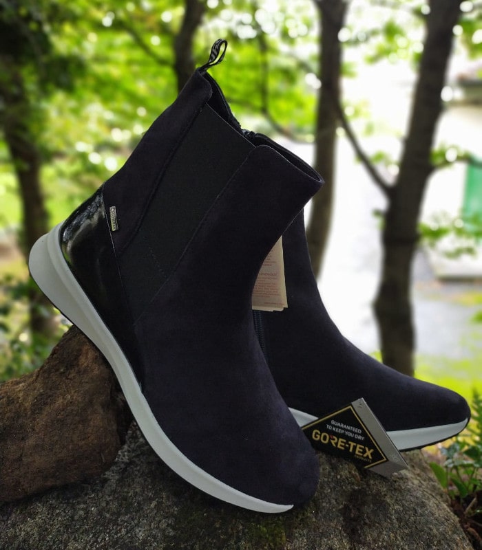 Botines deportivos impermeables con tecnología Gore-Tex en color negro con suela blanca, apoyados sobre una roca en un entorno boscoso