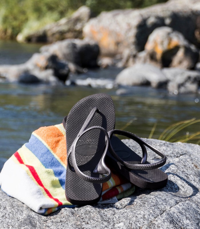 hanclas negras sobre toalla de rayas en una roca junto a un río, escena veraniega al aire libre con fondo de agua y vegetación